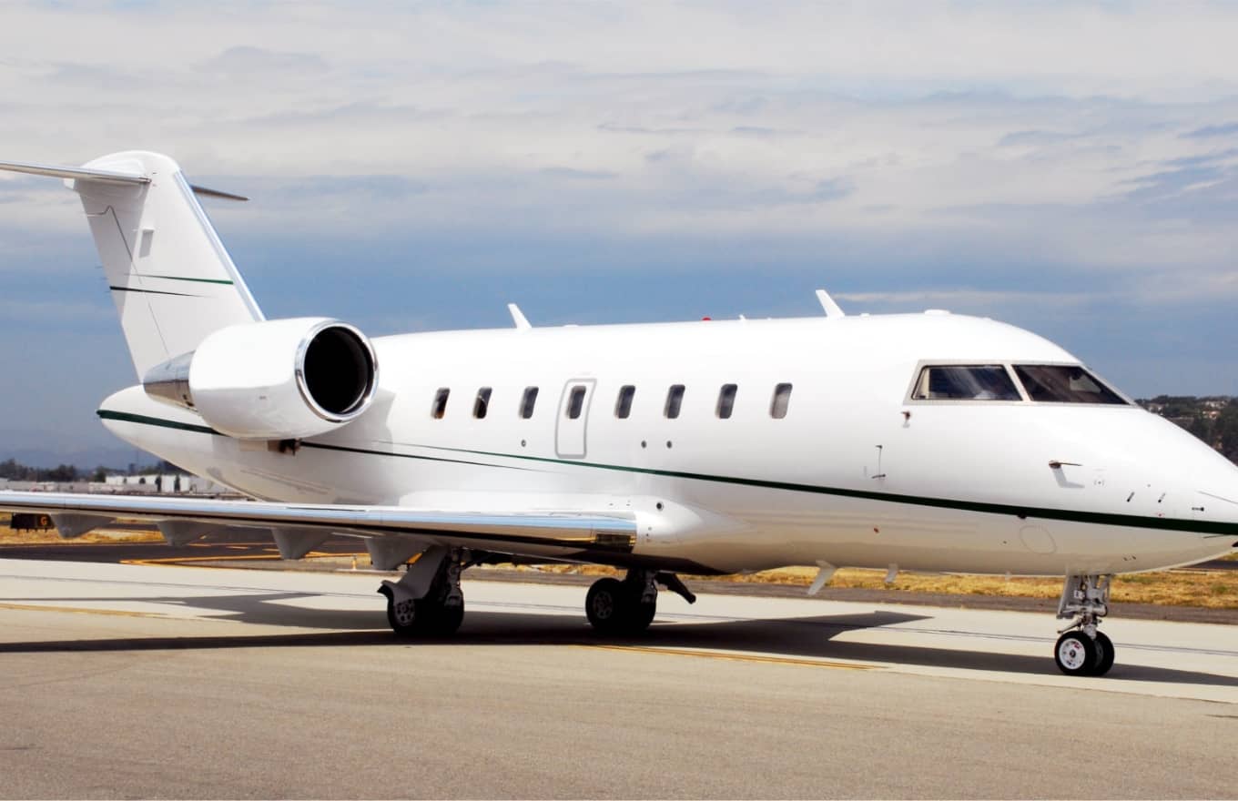 A white private jet with green stripes is parked on an airport runway under a partly cloudy sky.