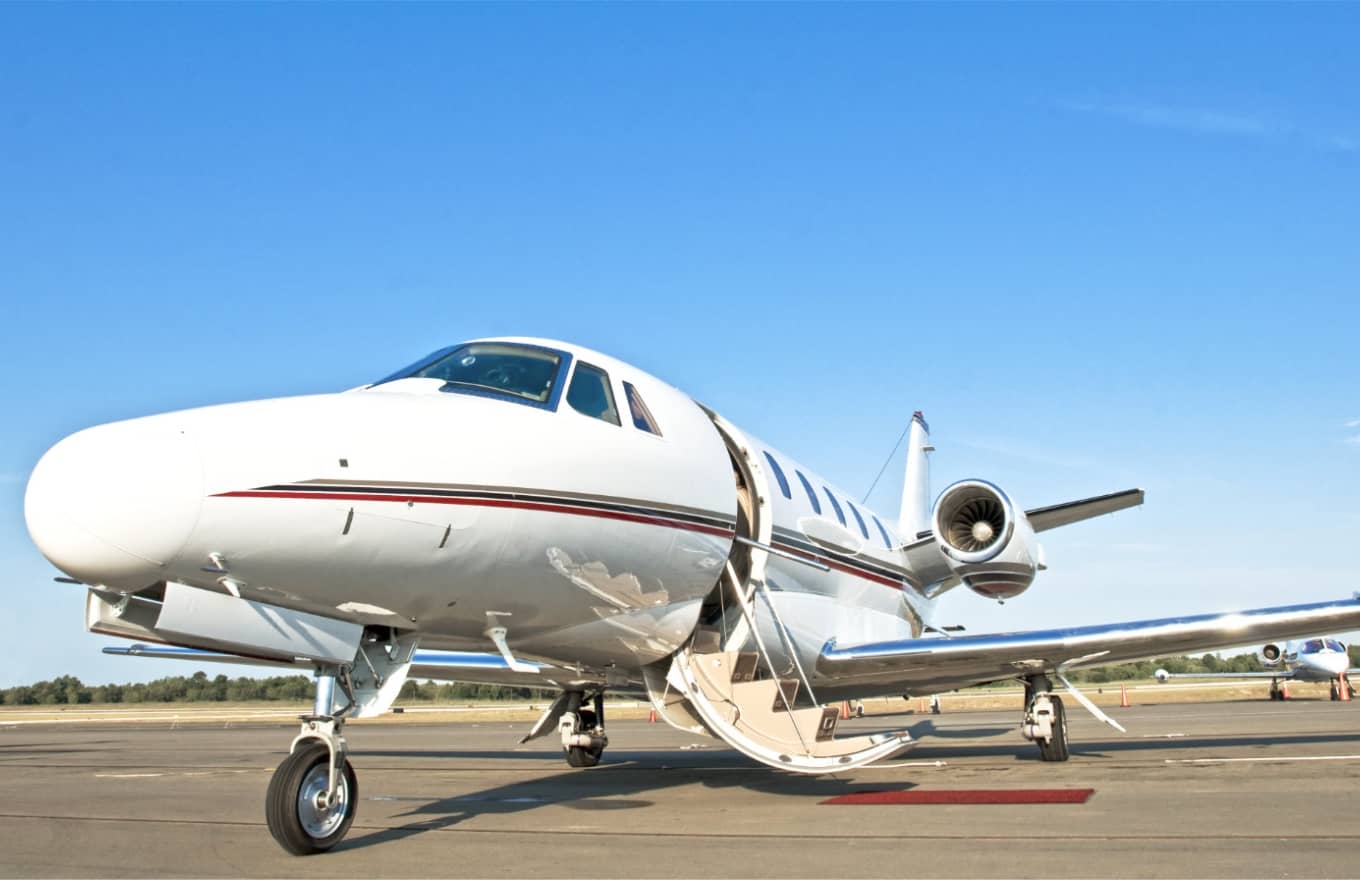 A white private jet with its door open is parked on an airport tarmac under a clear blue sky.