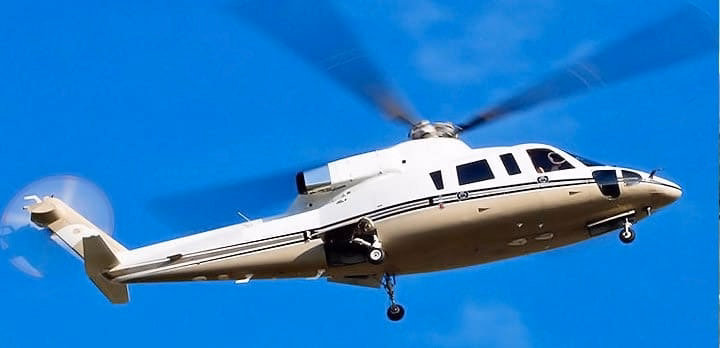 A white helicopter with dark stripes is flying against a clear blue sky, with its rotor blades in motion.