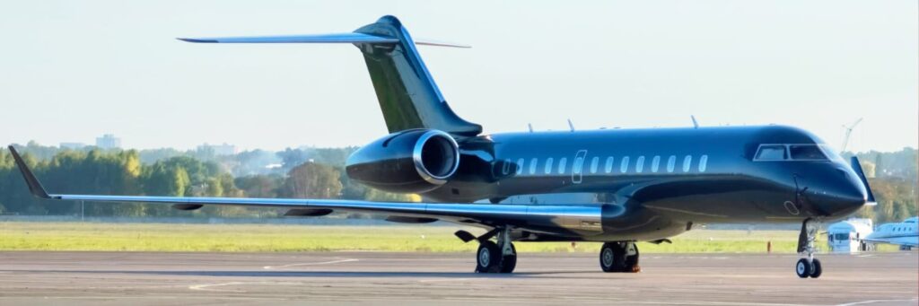 A black private jet is parked on an airport tarmac with a green landscape and city skyline in the background.