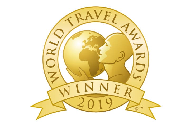 A gold badge with a globe and a stylized human figure, featuring the text "World Travel Awards Winner 2019" on it.